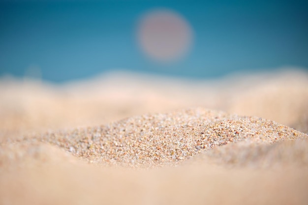 Close up of clean yellow sand surface covering seaside beach with blue sea water on background. Travel and vacations concept.