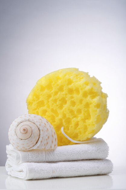 Close-up of cleaning sponge and towel by seashell on table in bathroom