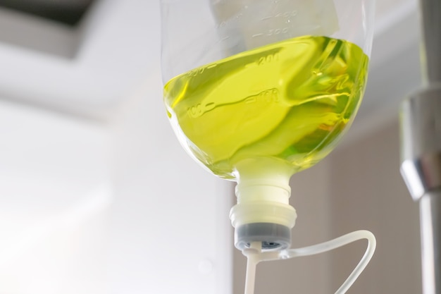 Photo close-up of a clear green saline bottle hanging on a stand for use with a patient.