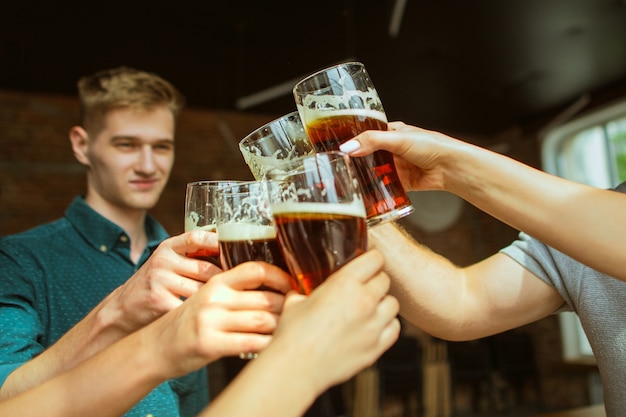 Foto primo piano tintinnante. giovane gruppo di amici che bevono birra, si divertono, ridono e festeggiano insieme. donne e uomini con bicchieri di birra. oktoberfest, amicizia, solidarietà, concetto di felicità.