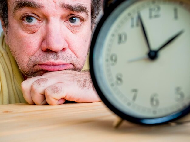 Foto close-up di un orologio contro un uomo triste sullo sfondo sul tavolo
