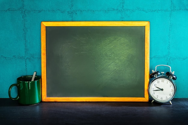 Photo close-up of clock with blank blackboard on table