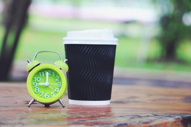 Photo close-up of clock with disposable cup on table