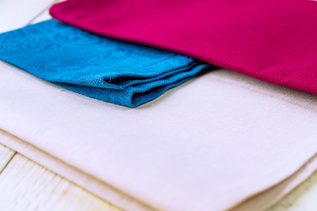 Close up of cloth napkins of beige, blue and burgundy colors on rustic white wooden table.