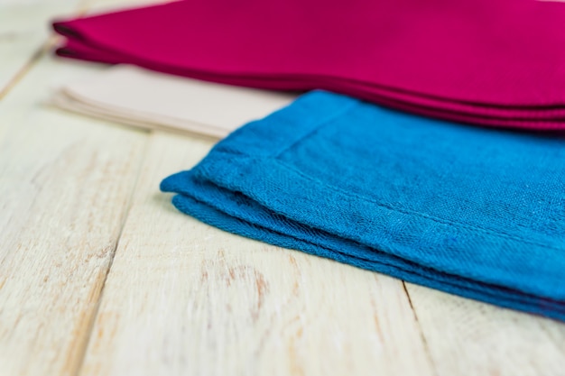 Close up of cloth napkins of beige, blue and burgundy colors on rustic white wooden table. 