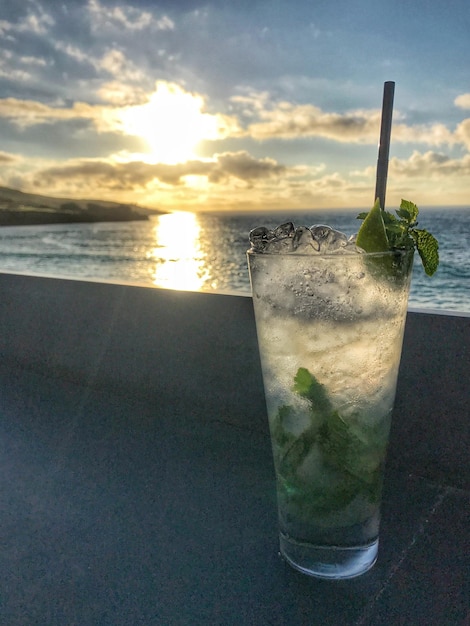 Photo close-up of cocktail on table against sea during sunset