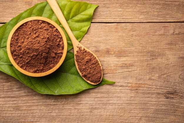 Close up Cocoa powder in wooden bowl and green leaf on wooden table