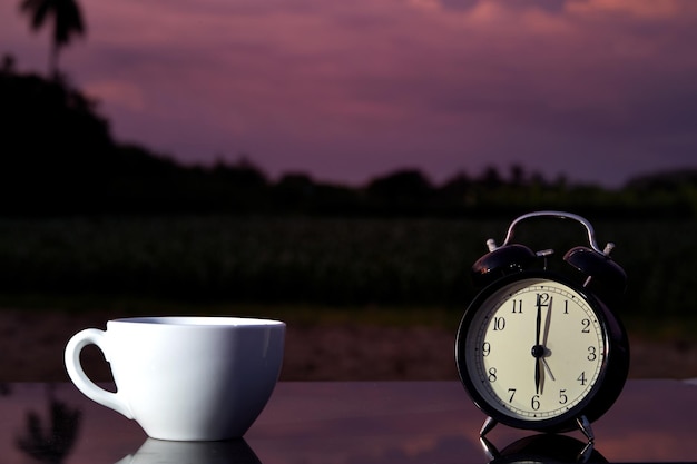 Close-up of coffee cup and alarm clock on table at sunset