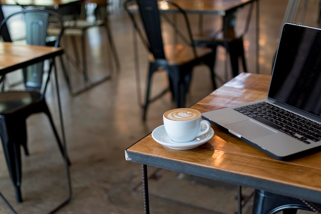 カフェのテーブル上のラップトップでコーヒーカップのクローズアップ