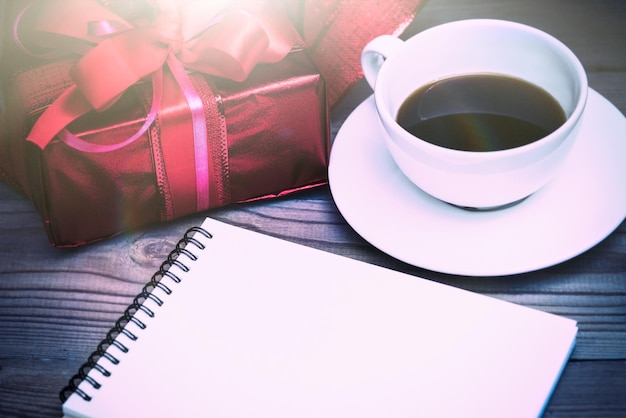 Photo close-up of coffee cup and gift by book on table