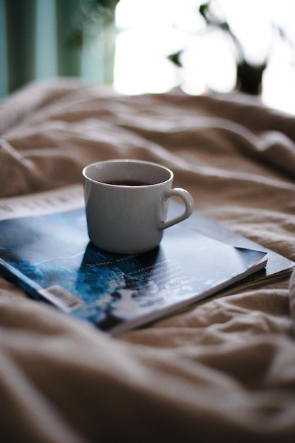 Close-up of coffee cup with books on bed