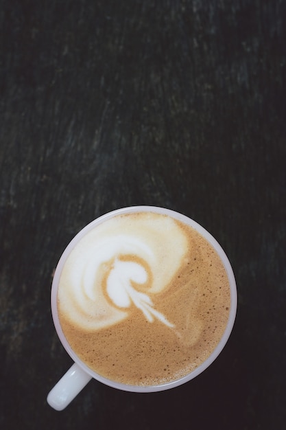 写真 朝の木製のテーブルで飲むカップと上記のミルクの泡でクローズアップコーヒーカフェラテアート。