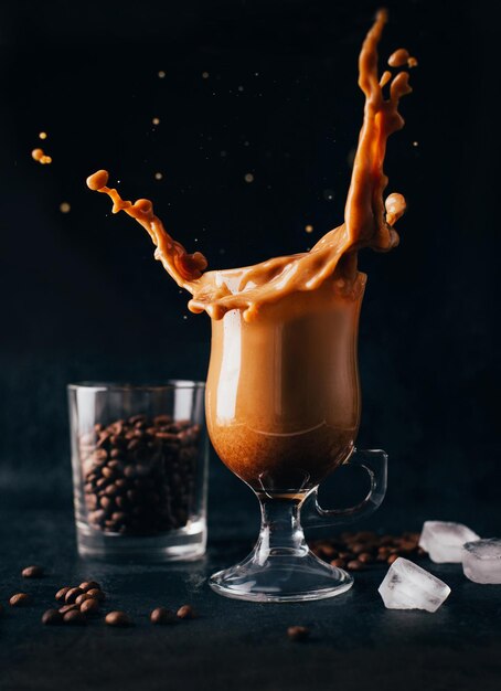 검정색 배경에 있는 커피 콩의 배경에 대해 투명한 유리에 우유를 넣은 커피 클로즈업
