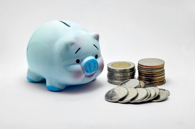 Foto close-up di monete da parte di un porcellino blu su sfondo bianco