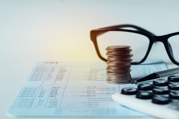 灰色の背景に対する銀行口座の硬貨と眼鏡のクローズアップ
