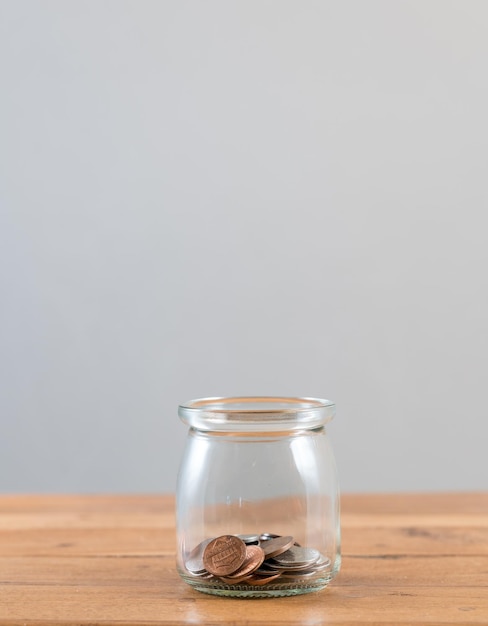 Photo close-up of coins in glass jar on table against gray background