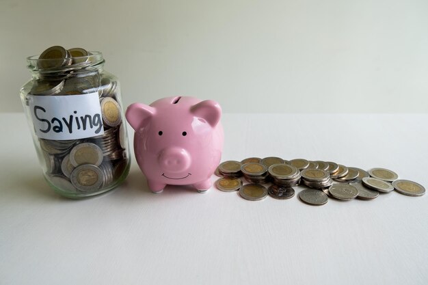 Close-up of coins with piggy bank and jar over white background