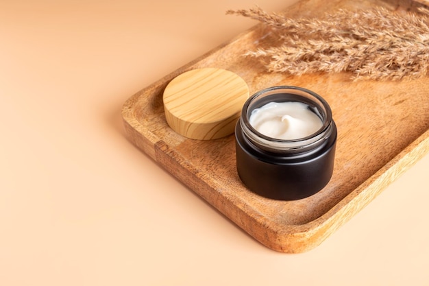 Photo close up of collagen cream in open black frosted glass jar and dry flowers reeds on beige background set for skin and body care beauty products space for text