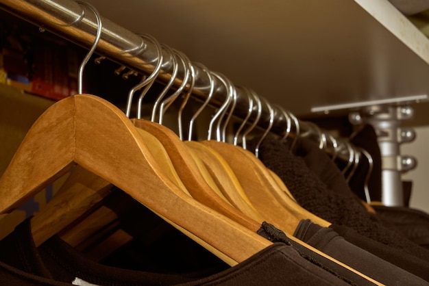 close up collection of black t-shirt hanging on wooden clothes hanger in closet