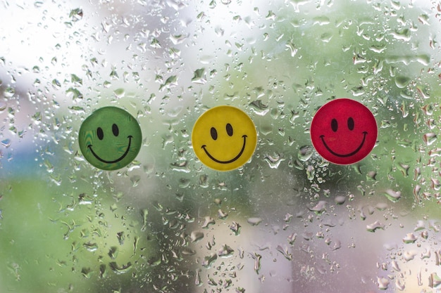 Photo close-up of colorful anthropomorphic smiley faces on wet window