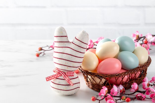 Close up of colorful Easter eggs in the nest with pink plum flower on bright white wooden table.