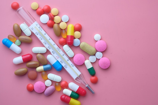 close up of colorful pills and thermometer on pink background