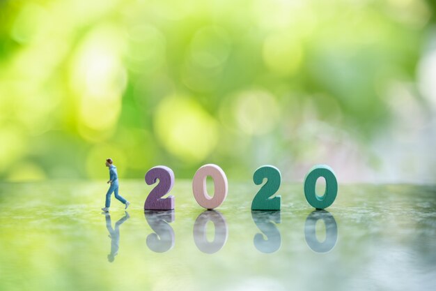 Close up of colorful wooden number 2020 on ground with runner miniature figure run to left side and bokeh green leaf nature .