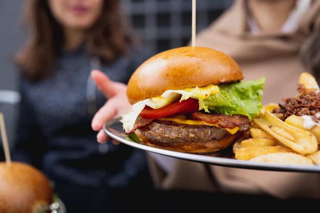 Close-up combomenu met gastronomische hamburger en frietjes met saus op tafel. Onherkenbare vrouw op achtergrond