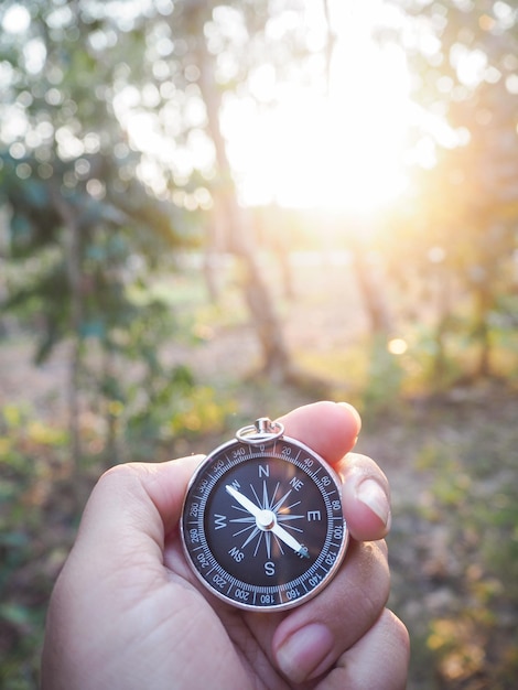 Close up of compass in woman hand with forest in the sunset time as background The concept of world tourism day Searching the right directions and Travel