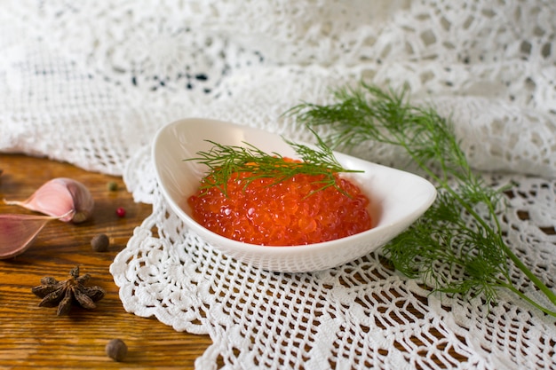 Photo close up composition white bowl with red caviar and dill on old wooden table. healthy food. fish appetizer.