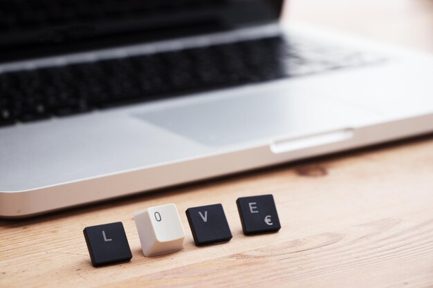 Photo close-up of computer keys with love text by laptop on table