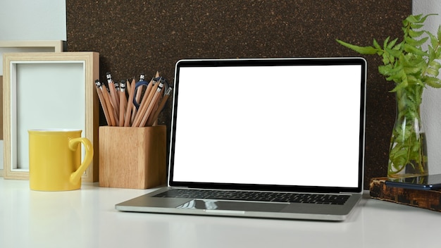 Close-up computer laptop met leeg scherm, potlood houder, koffiekopje en kamerplant op witte tafel.
