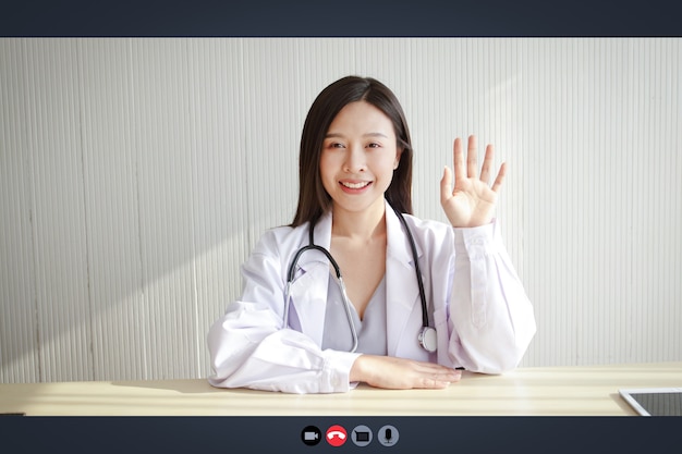 Close-up on a computer screen, a beautiful asian woman doctor\
treats a patient via online video call