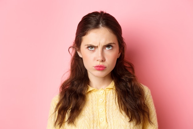 Photo close up of confused and perplexed young s woman frowning puzzled looking up cant understand something standing gloomy against pink wall