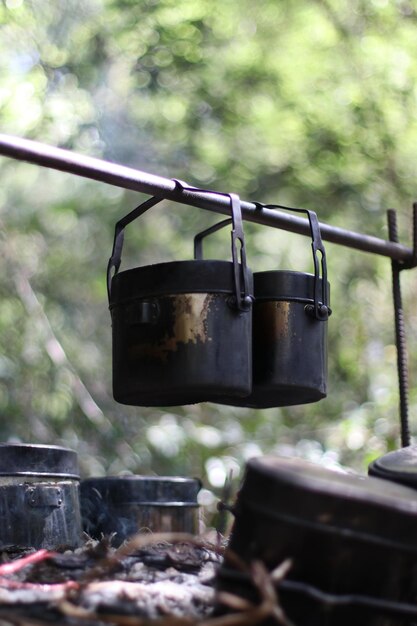 Close-up of containers hanging over bonfire in forest