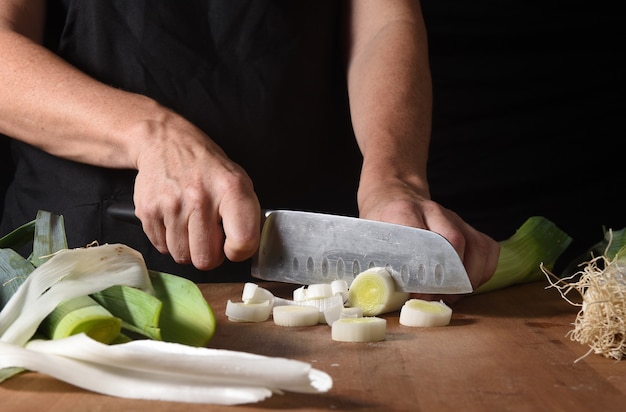 Close up  of a cook cutting a leek on wood