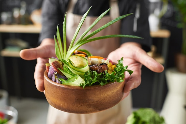 野菜とレタスの葉で飾られた肉と料理を保持している料理人のクローズアップ