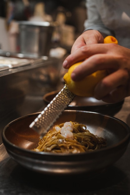 Close up of a cook's hand grating lemon over a tagliatelle pasta dish at a italian restaurant