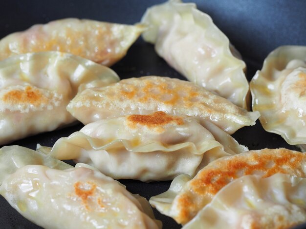 Close up cooking fried dumplings in a frying pan. Chinese food with hot steams, on rustic vintage wooden background.