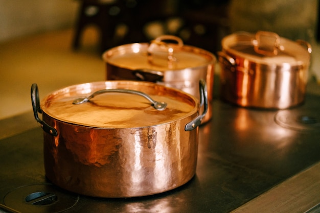 Close-up of copper pots with closed lids on an antique burner stove