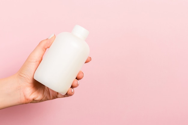 Close up of cosmetics bottle in female hand at pink