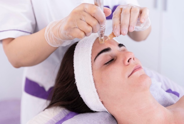 Photo close up of cosmetologistbeautician applying facial dermapen treatment on face of young woman customer in beauty saloncosmetology and professional skin care face rejuvenation