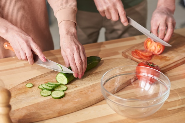 Primo piano della coppia che taglia cetriolo fresco e pomodoro sul tagliere per insalata