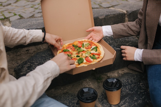 Close-up of Couple grab slices of pizza from box at the outdoor