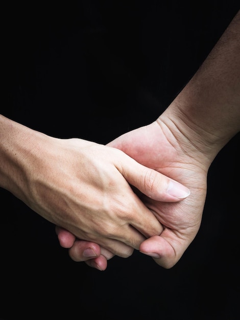 Foto close-up di una coppia che si tiene per mano su uno sfondo nero