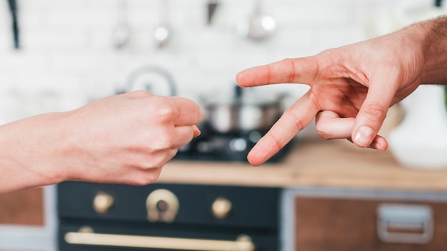 Foto primo piano delle coppie che giocano il gioco delle forbici di carta della roccia nella cucina