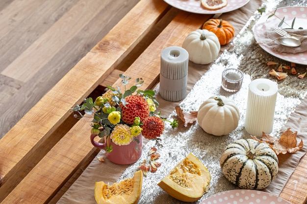 Close-up of cozy decor details of a festive autumn dining table with pumpkins, flowers and candles.