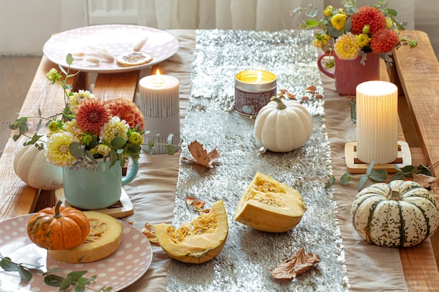 Close-up of cozy decor details of a festive autumn dining table with pumpkins, flowers and candles.