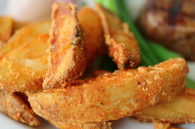 Close-up di croccanti patate fritte con verdure sfocate e bistecca in background