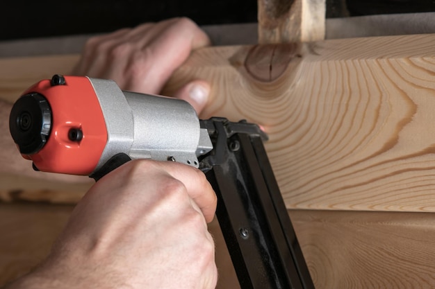 Close up cropped carpenter male hands use pneumatic nailer stapler gun for wood timber plank Craftsmanship handcraft